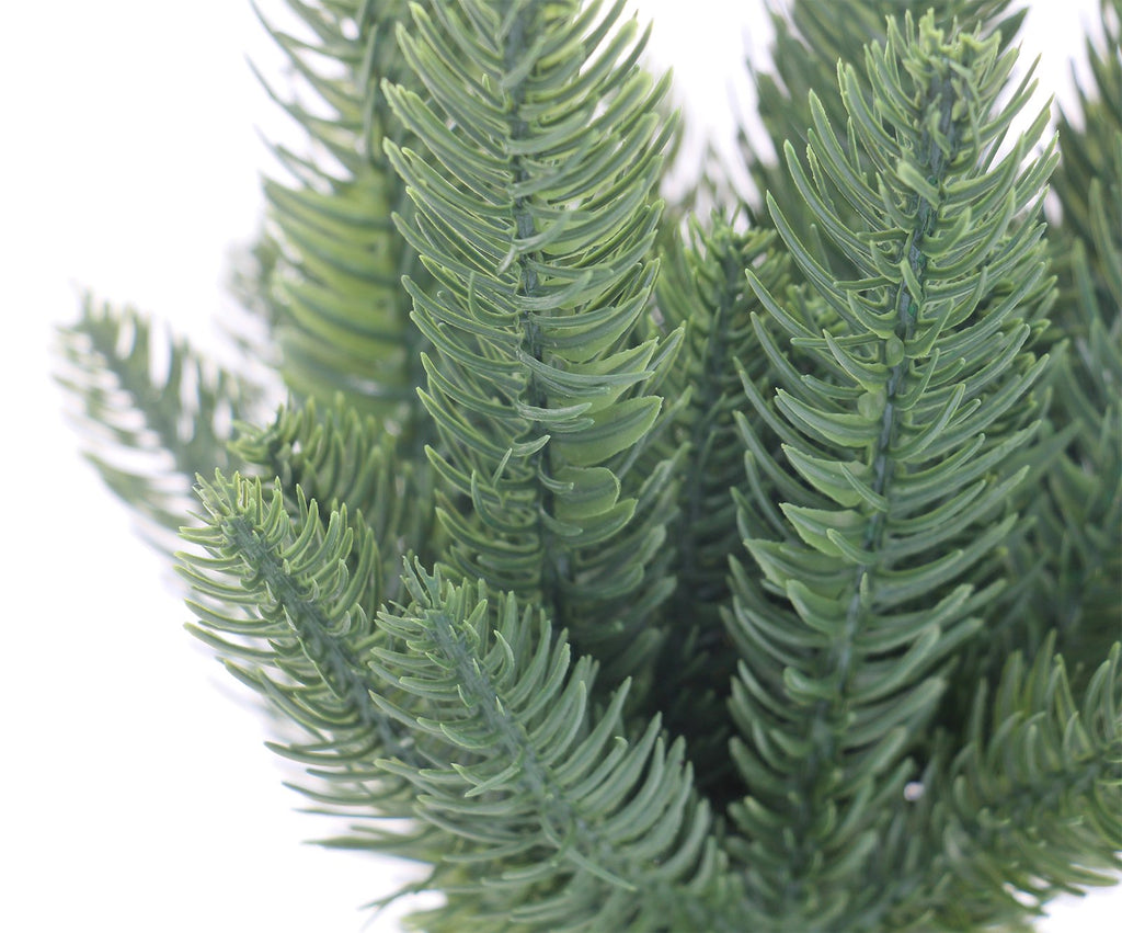 Close-up of artificial green pine branches with detailed needles against a white background.