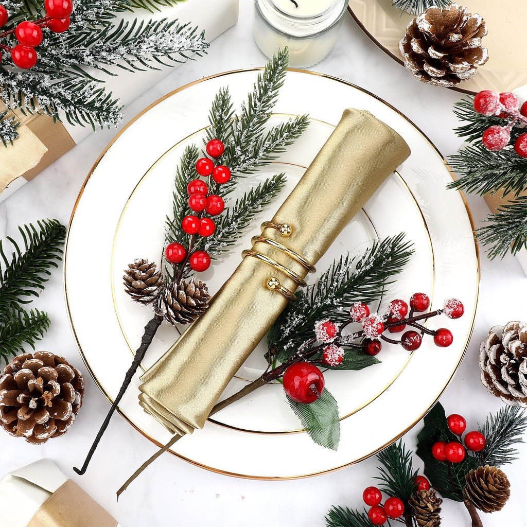 Christmas floral picks with faux cedar, pine needles, red berries, and pinecones arranged on a white plate with a gold rim, holding a gold napkin.
