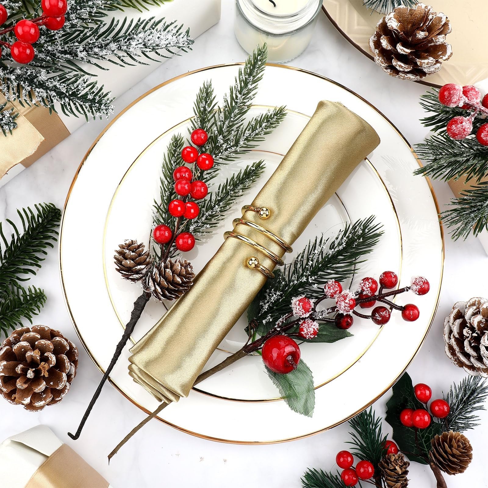 Christmas floral picks with faux cedar, pine needles, red berries, and pinecones arranged on a white plate with a gold rim, holding a gold napkin.