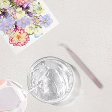 Dried pressed flowers and leaves kit with tweezers and resin in a bowl, flat lay overhead view.