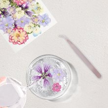 Dried pressed flowers and leaves being placed into clear resin with tweezers