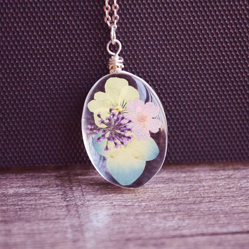 Oval pendant with dried flowers and leaves encased in clear resin, hanging from a silver chain.