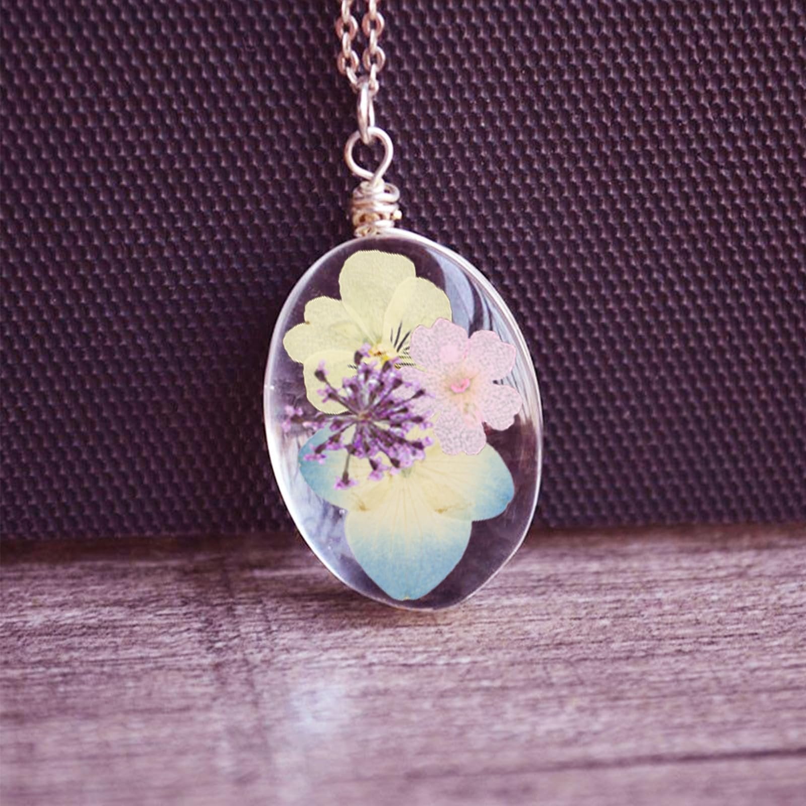 Oval pendant with dried flowers and leaves encased in clear resin, hanging from a silver chain.