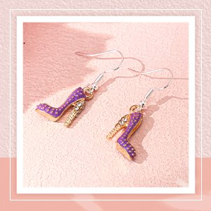 Purple high heel charm earrings with gold accents and rhinestones, displayed on a pink textured surface.
