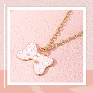 Pink and white polka dot bow necklace pendant on a gold chain, close-up shot on a textured pink surface.
