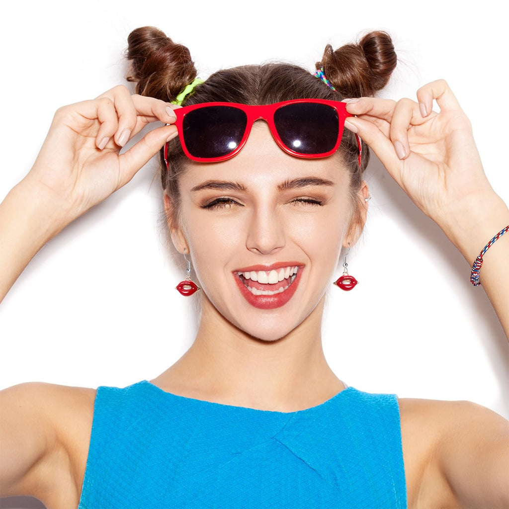 Woman with red sunglasses and lip-shaped earrings winking and smiling, wearing a blue top