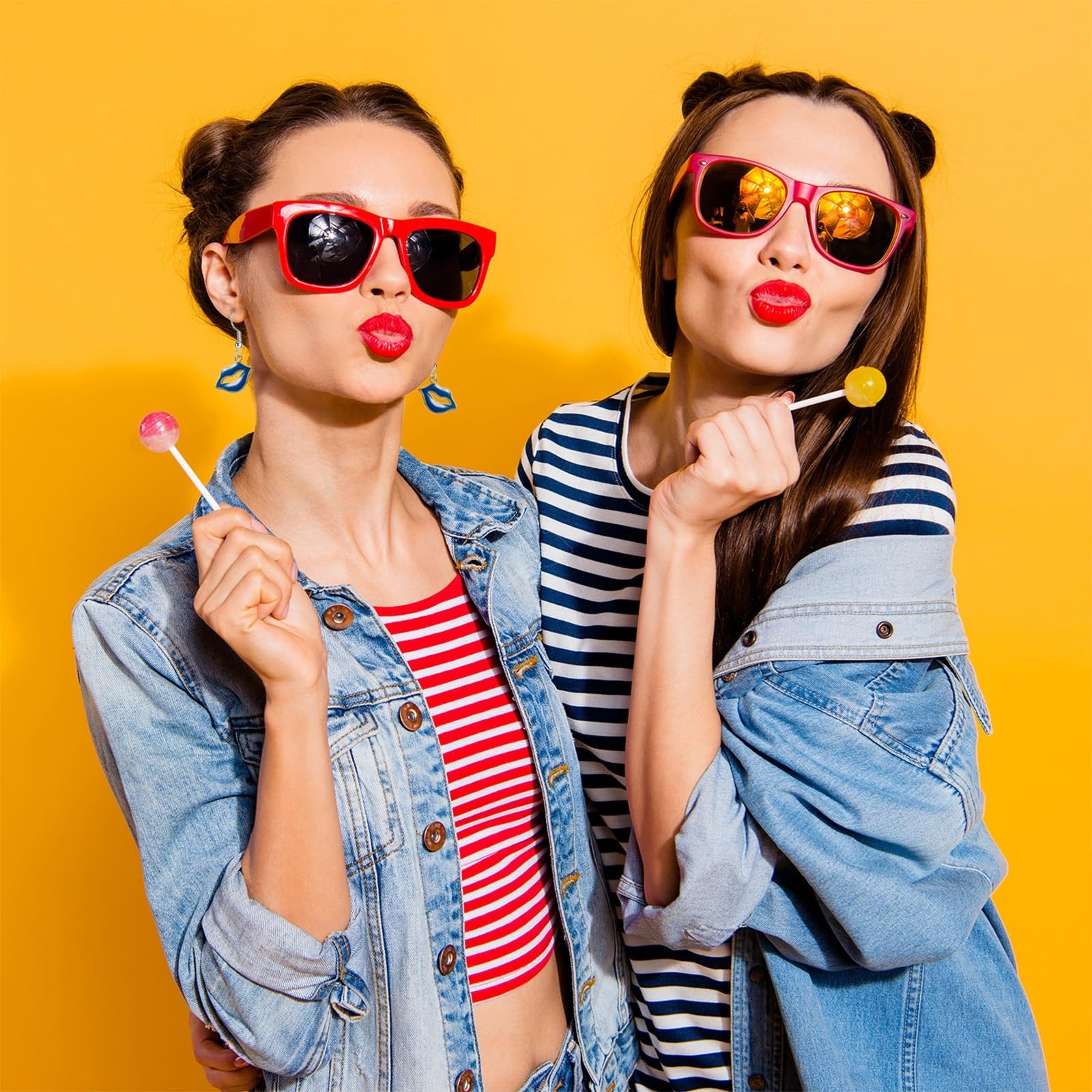 Two young women with buns in their hair wearing sunglasses and denim jackets, holding lollipops.
