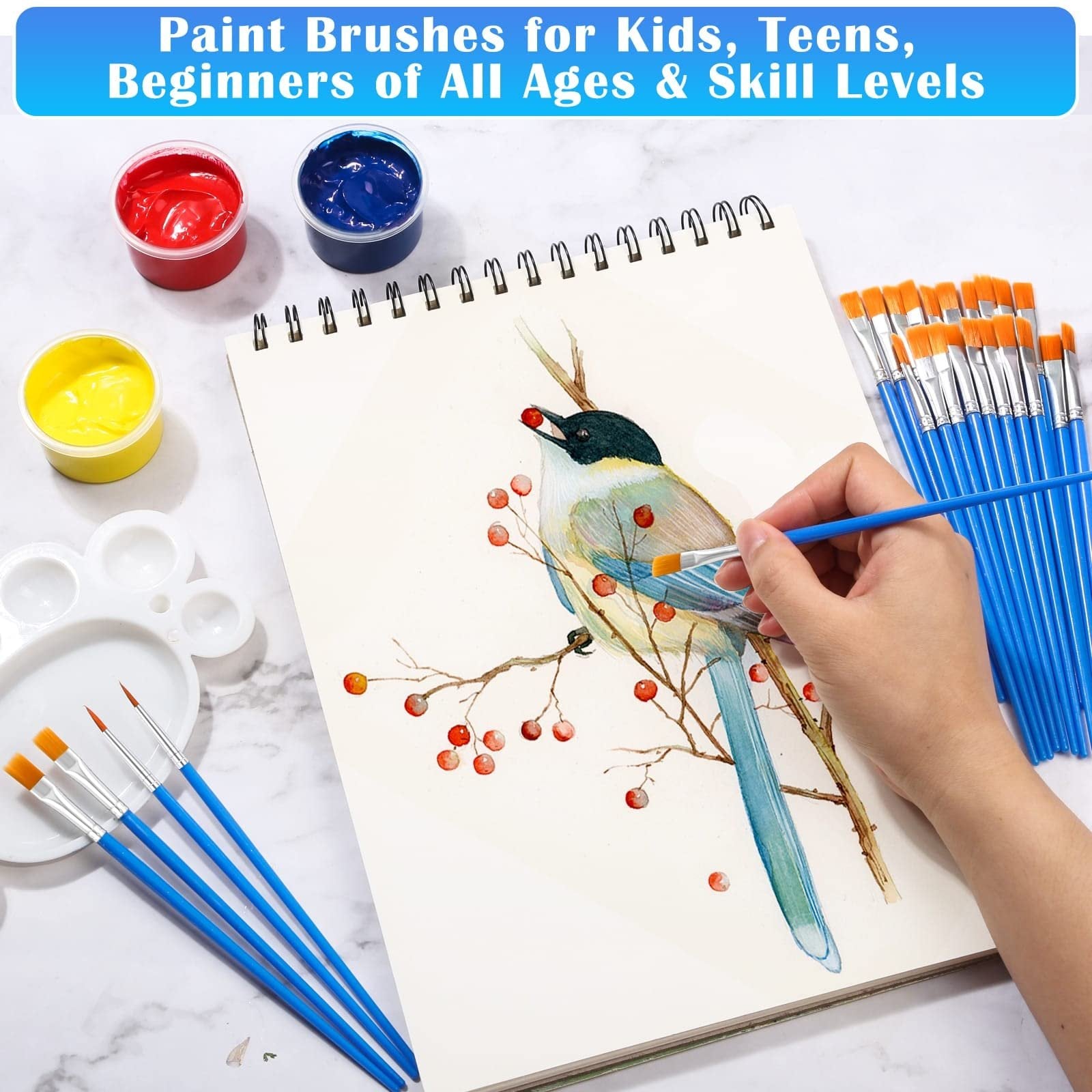 A hand paints a bird on a sketchpad with a blue-handled brush, surrounded by paint pots and brushes.