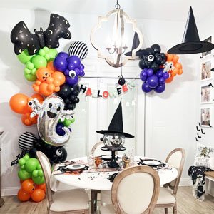 Halloween balloon decorations including ghosts, bats, and pumpkins, arranged around a dining table set for a party.