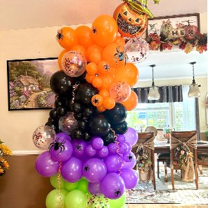 Halloween balloon arch in black, orange, purple, and green with spider and pumpkin accents, set up indoors.