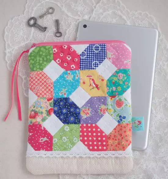 Quilted fabric pouch with assorted patterns next to a tablet, with vintage keys on lace.