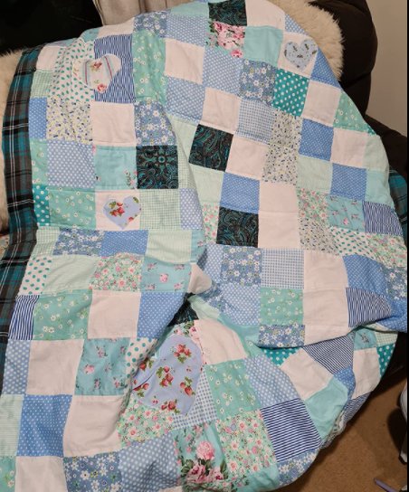 Quilt made of assorted blue, white, and teal fabric squares with floral and heart appliques, draped over furniture.