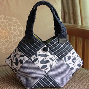 Patchwork tote bag with braided handles and button closure, featuring various blue and white fabric patterns.