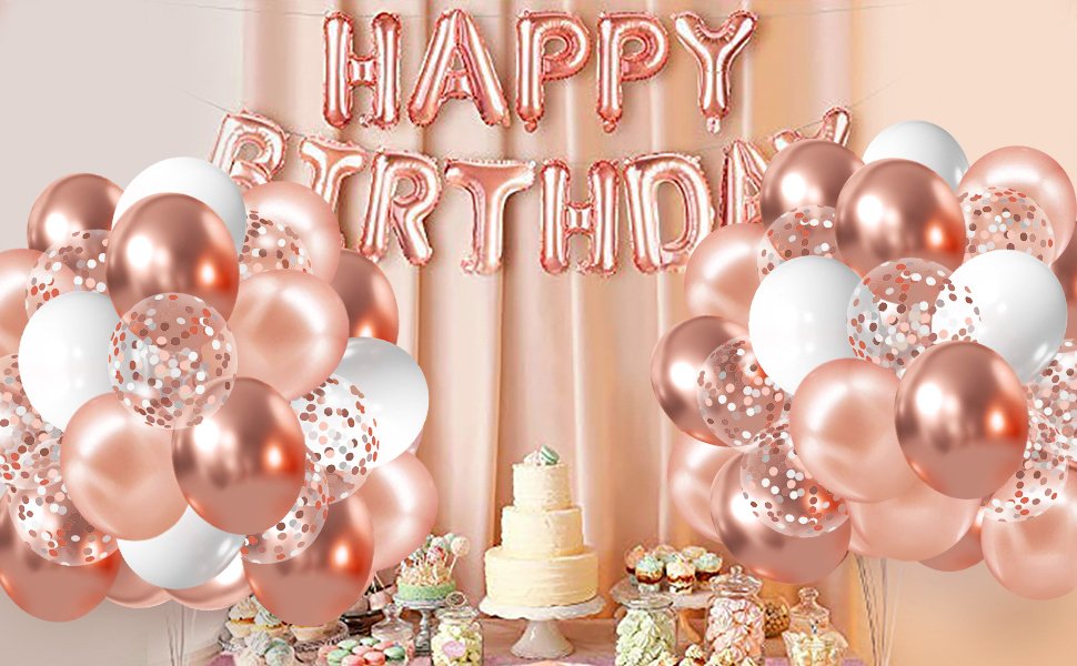 Rose gold, white, and confetti balloons arranged around a tiered cake and desserts with a 'HAPPY BIRTHDAY' banner in the background.