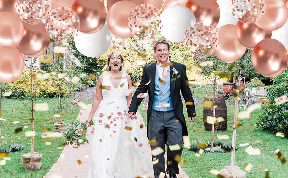 Bride and groom walking down a path with rose gold, confetti, and white balloons overhead and confetti falling.