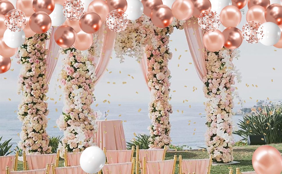 Rose gold, white, and confetti balloons float above a wedding ceremony arch decorated with flowers.