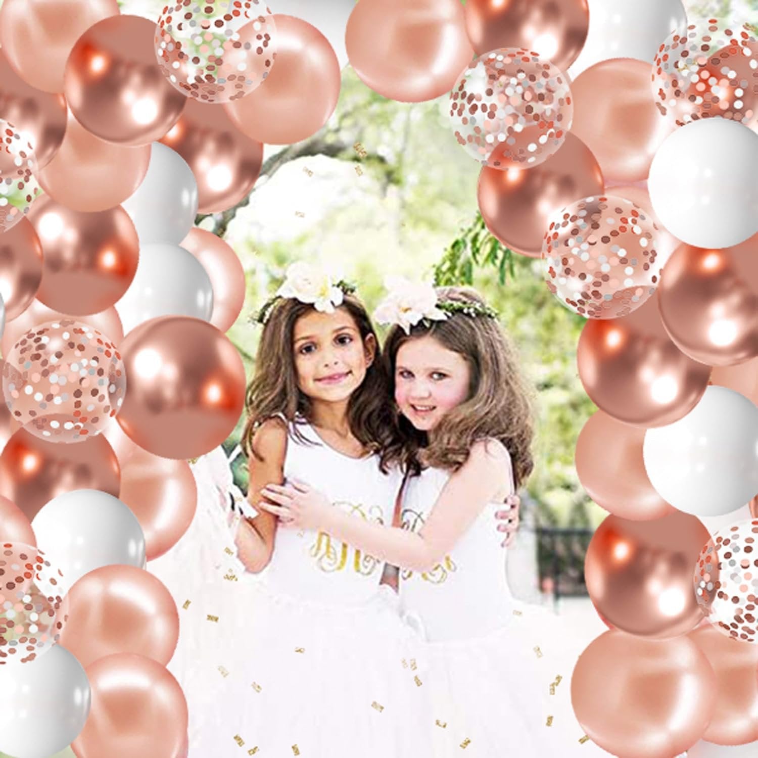 Two young girls in white dresses wearing flower crowns, surrounded by rose gold, white, and confetti balloons.