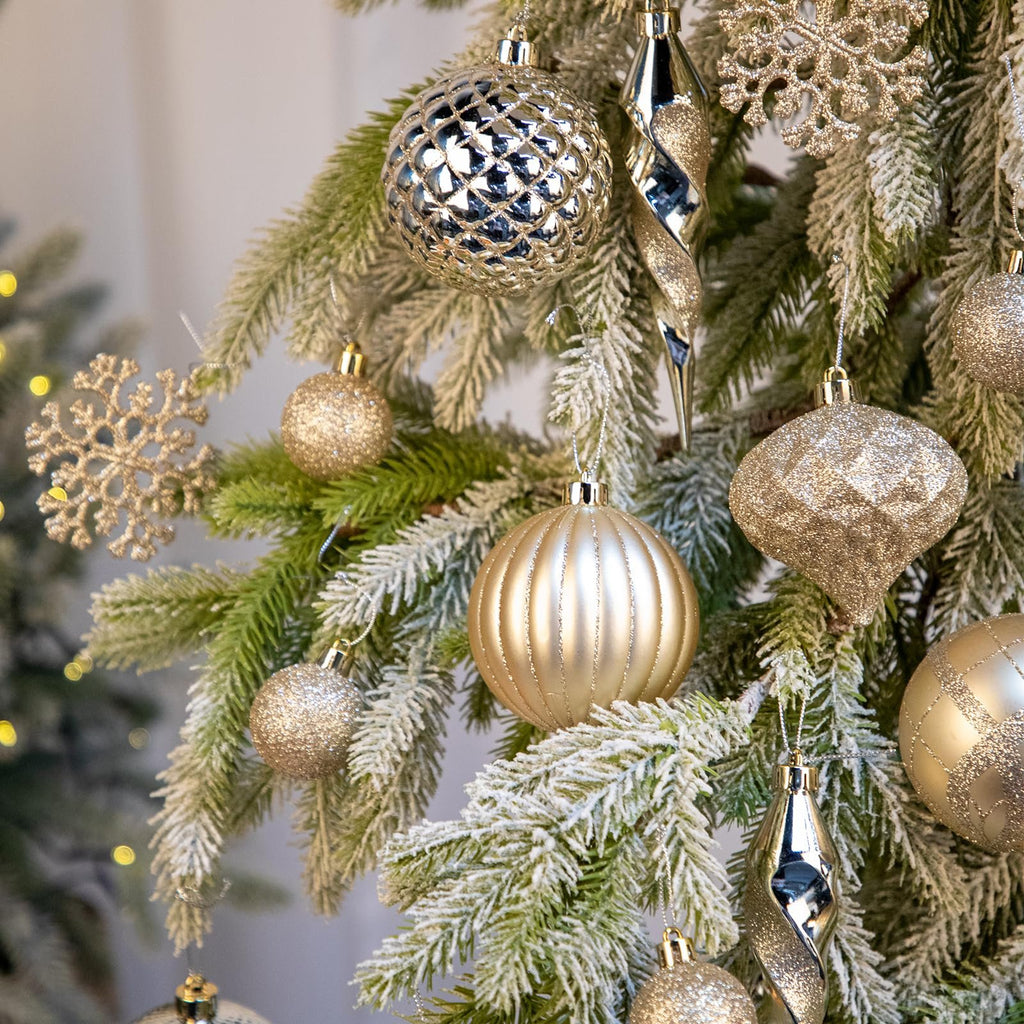 Champagne colored Christmas ornaments including balls, icicles, and snowflakes hanging on a frosted tree branch.