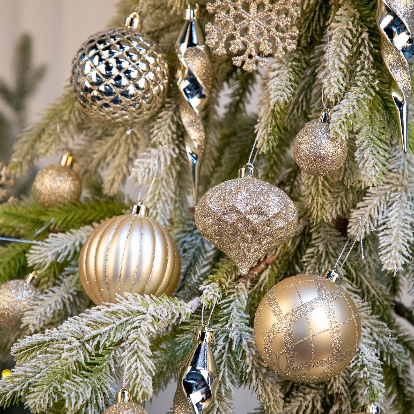 Champagne colored Christmas ornaments including balls, icicles, and a snowflake hanging on a frosted tree branch.