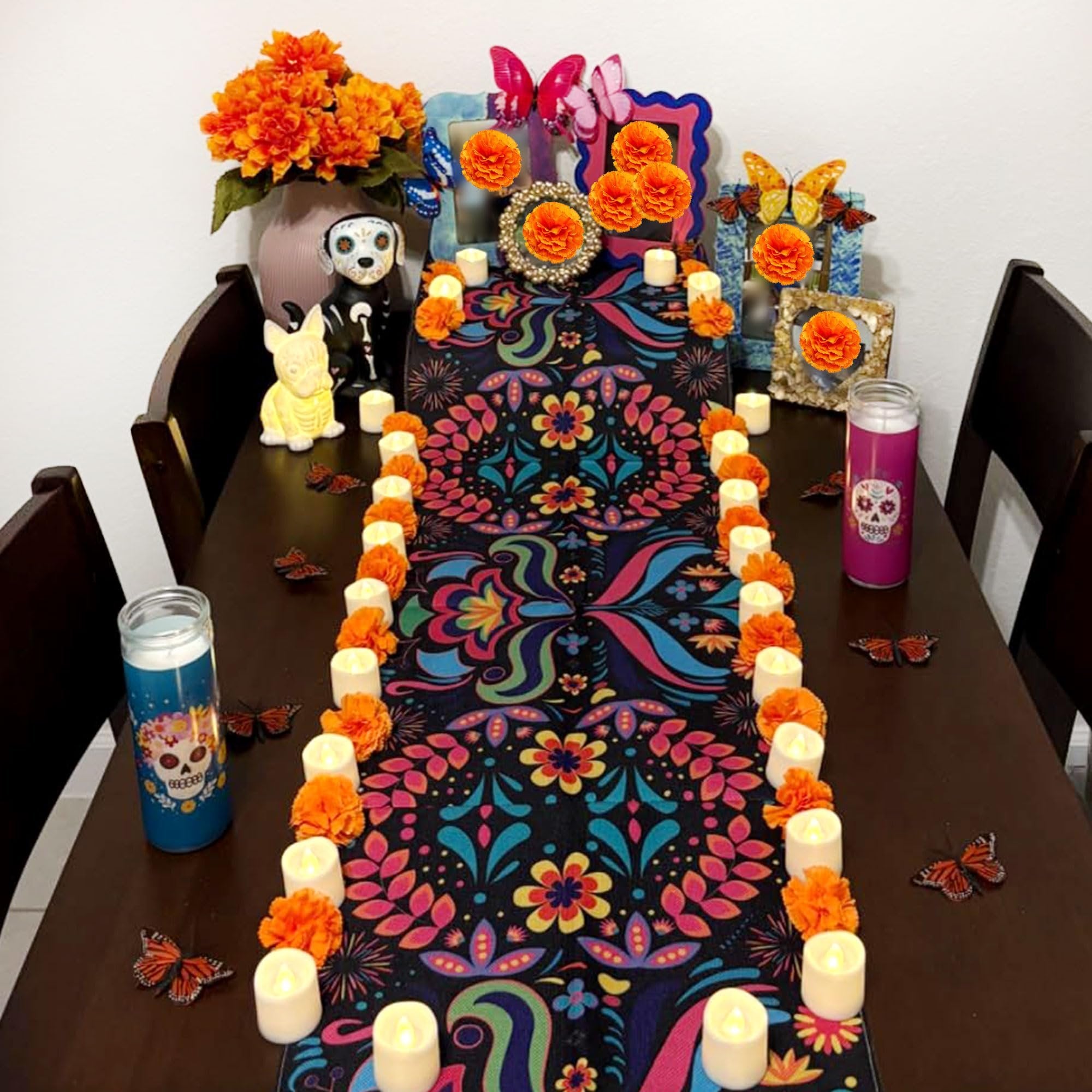 Table decorated for Day of the Dead with orange marigold flowers, candles, butterflies, and a colorful runner.