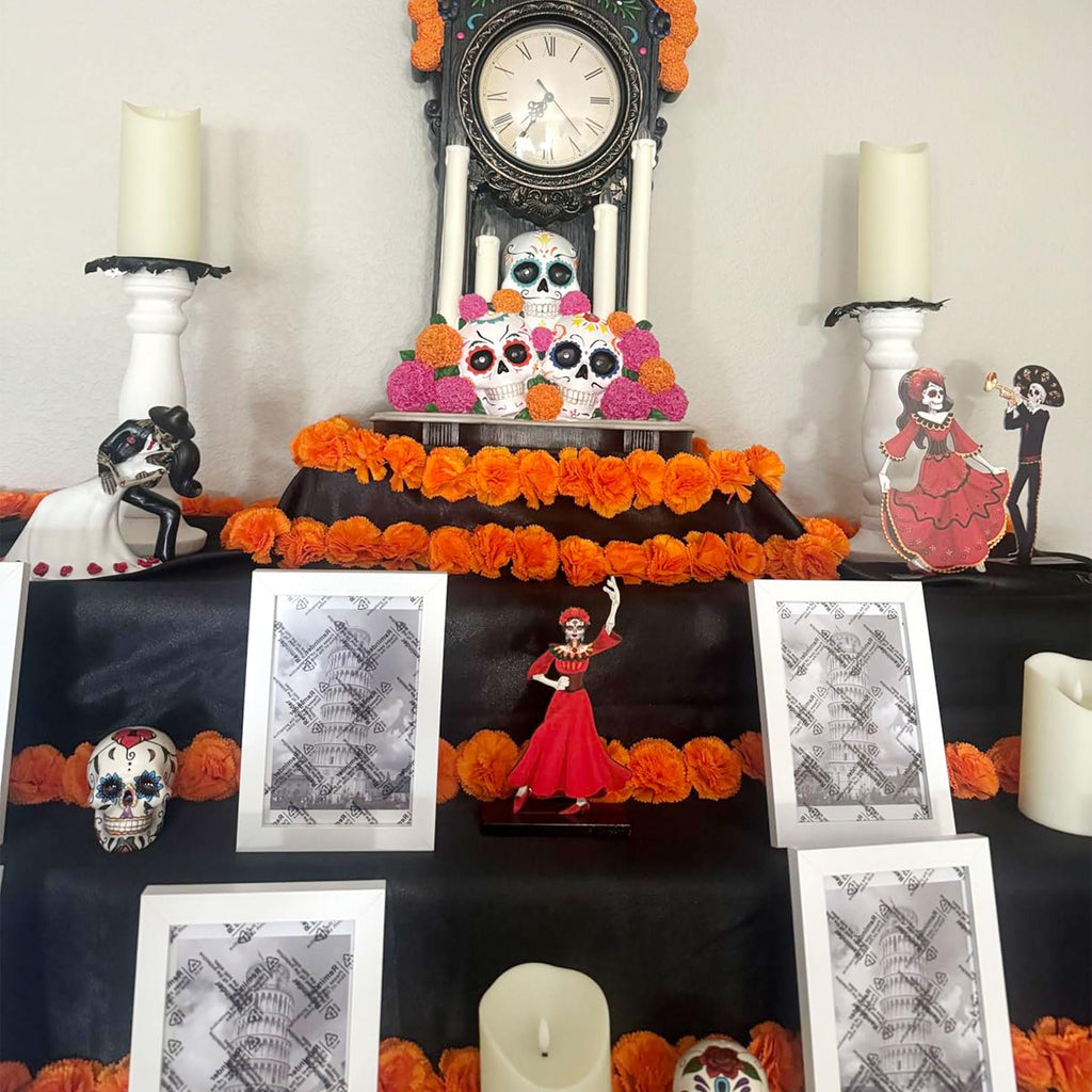 Day of the Dead altar setup with skulls, marigold garlands, candles, and framed photos of the Leaning Tower of Pisa.