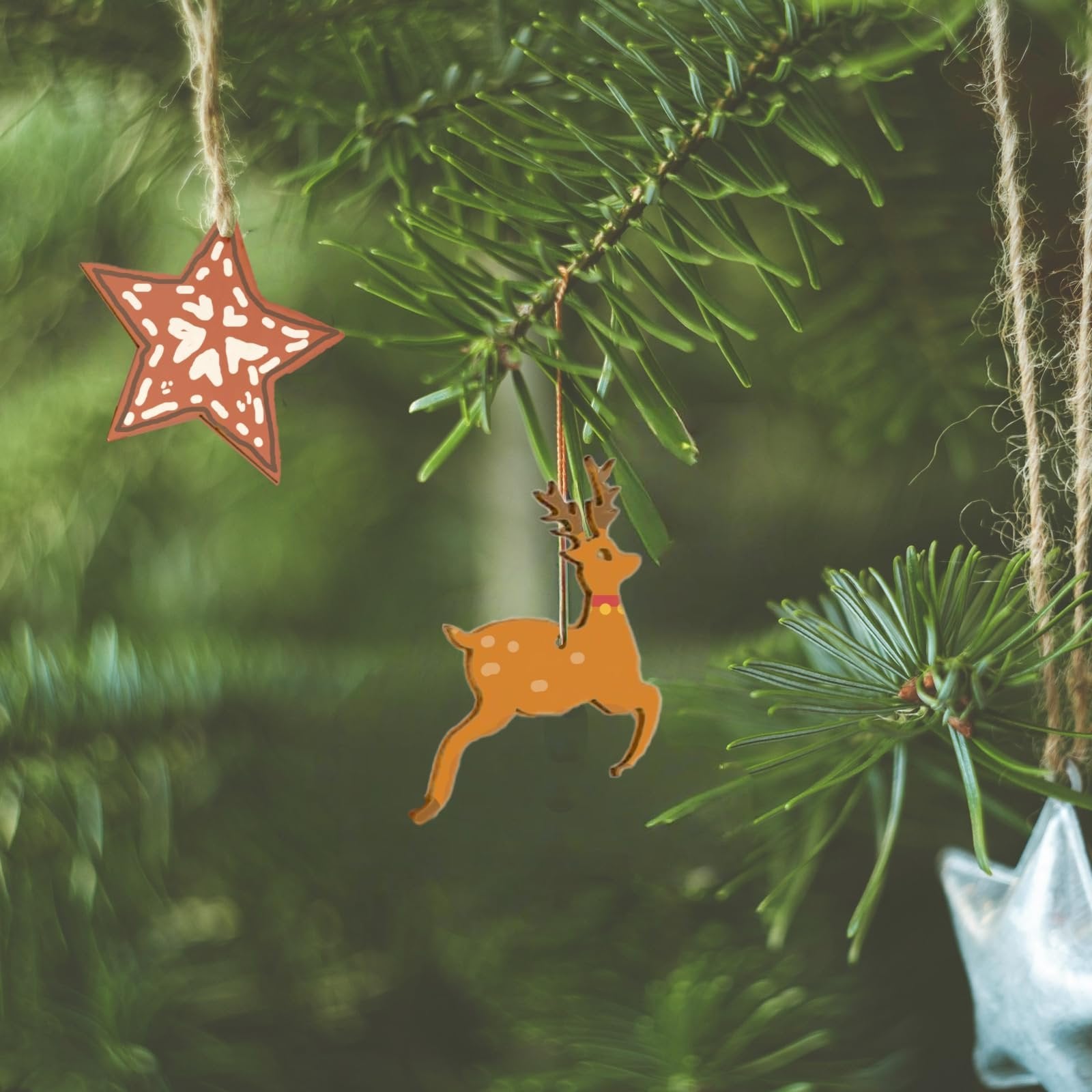 Close-up of unfinished wooden Christmas ornaments, including a star and a reindeer, hanging on a pine tree branch.