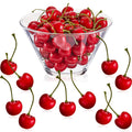 Artificial red cherries in a clear bowl and scattered around, with stems