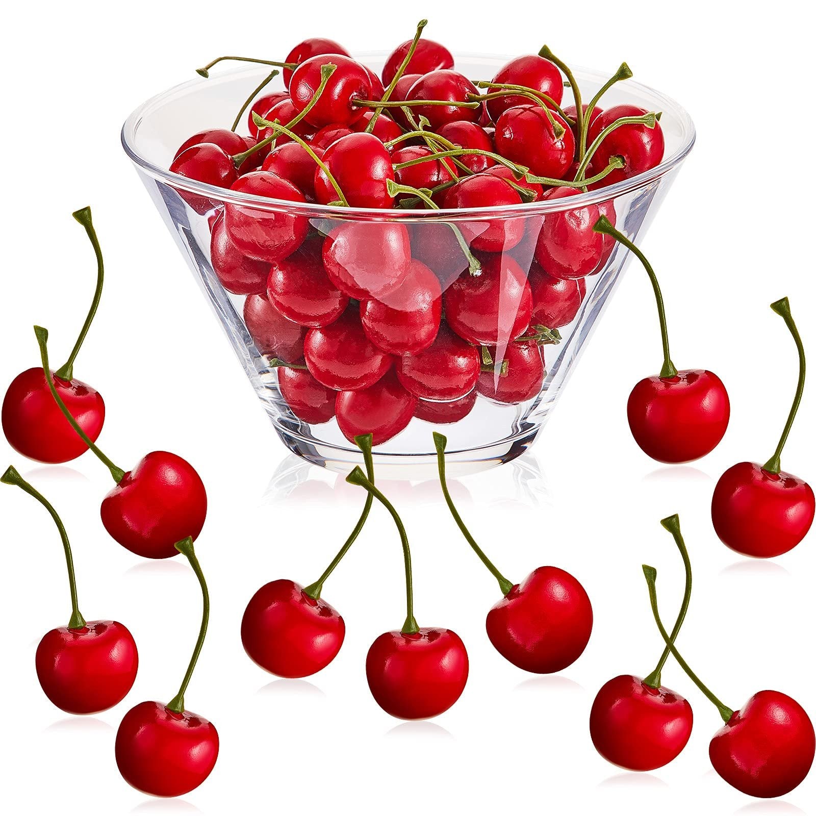 Artificial red cherries in a clear bowl and scattered around, with stems