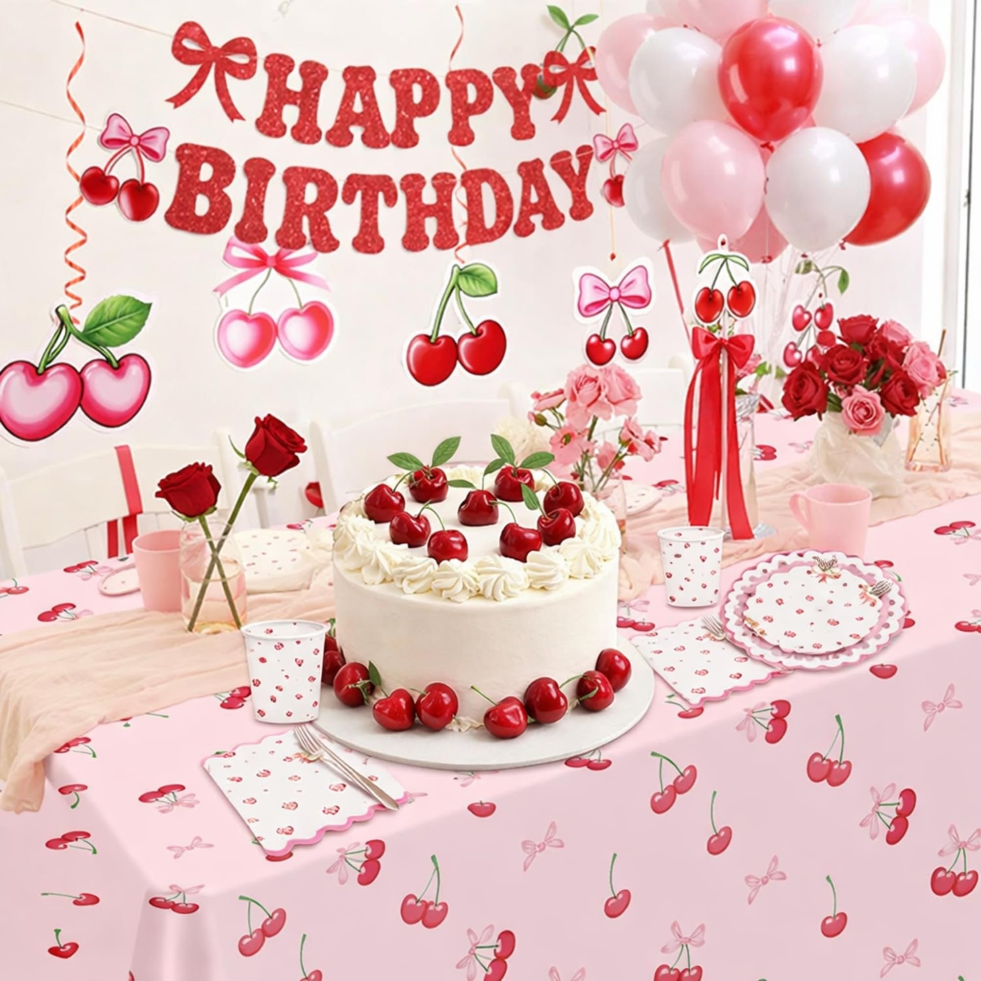 Birthday party table setting with a cake decorated with artificial cherries, balloons, and cherry-themed tableware.