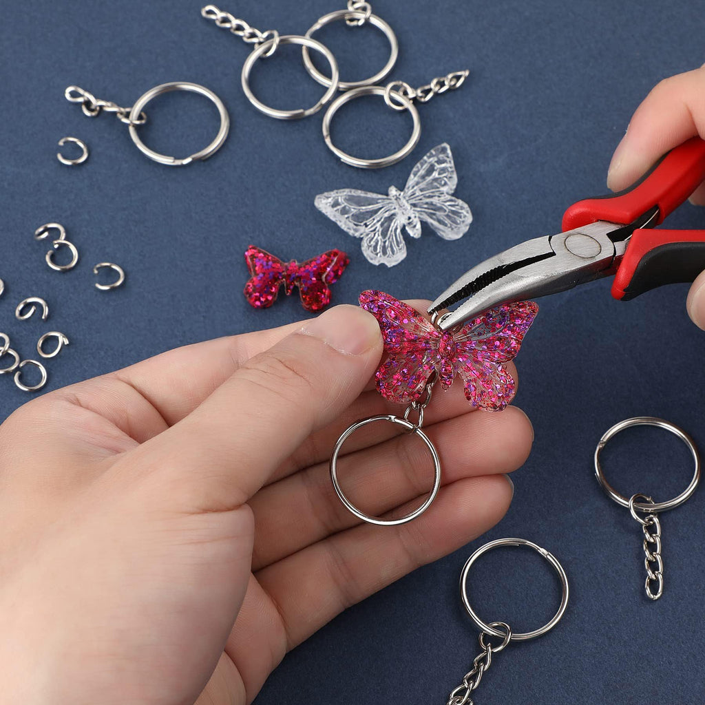 Hands using pliers to attach a glittery pink butterfly charm to a silver keychain ring with a chain.