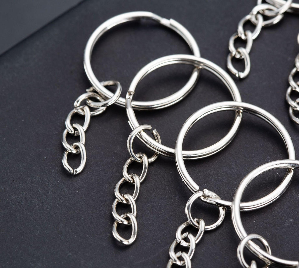 Silver split round keychain rings with chains and jump rings on a dark surface, close-up view.