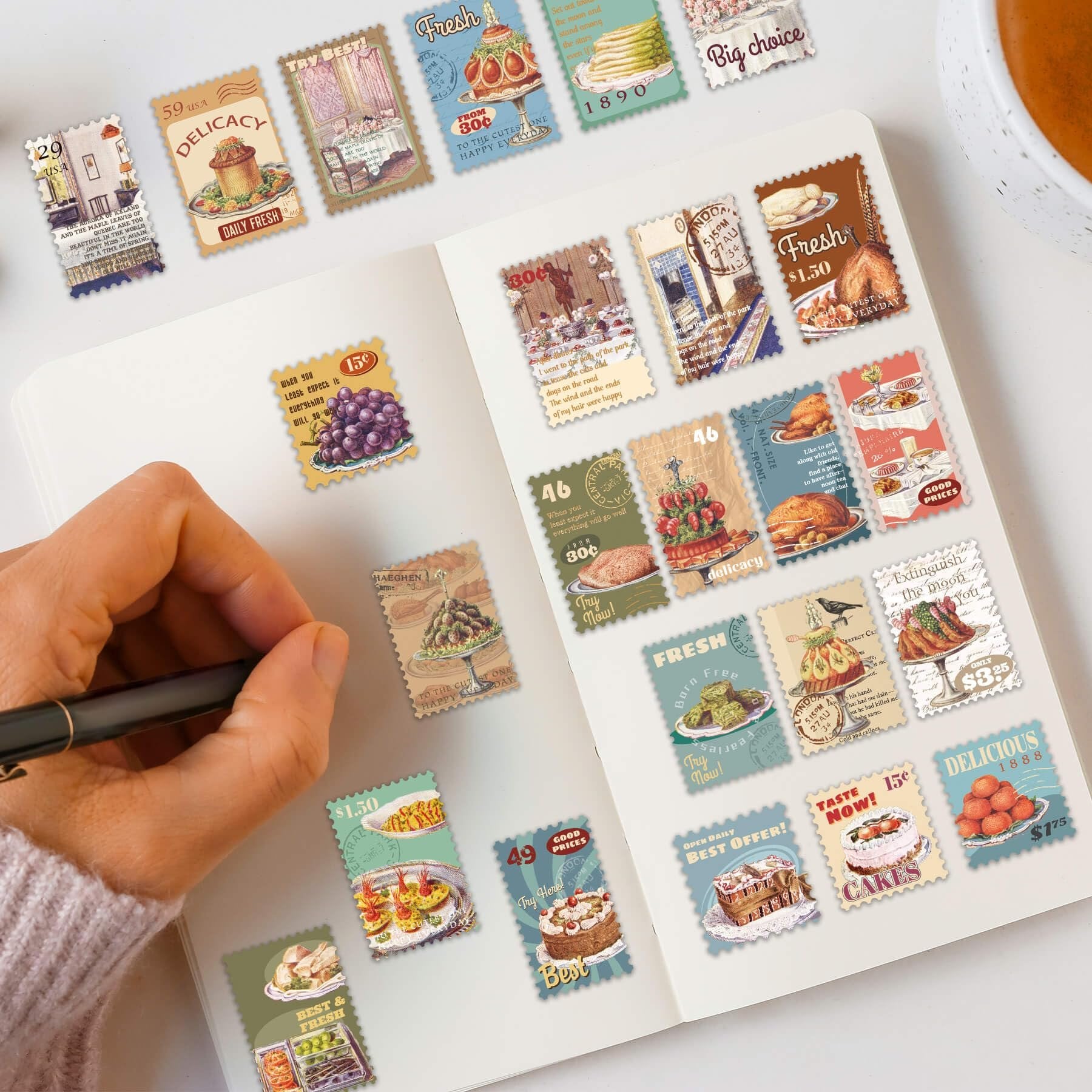A hand holding a pen over a notebook filled with vintage food postage stamp stickers. The stickers feature various food items like cakes, grapes, and roasted chicken.