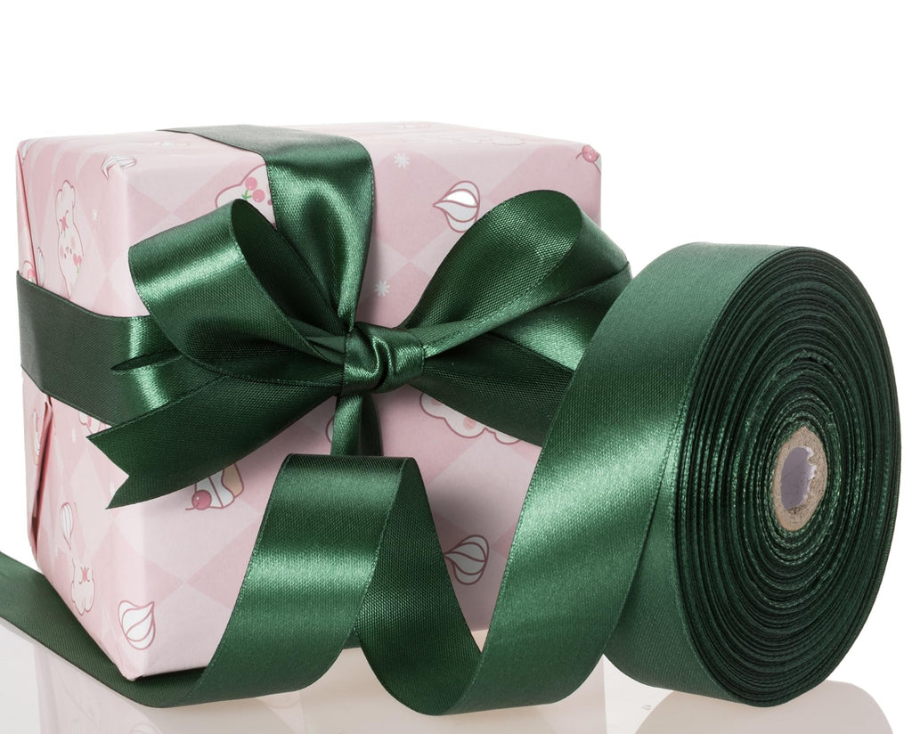 Forest green satin ribbon wrapped around a pink gift box with a bow, and a roll of ribbon.