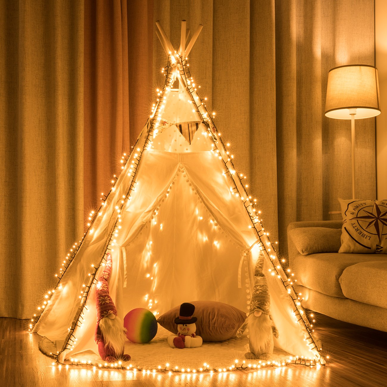 White teepee tent decorated with warm white string lights, with gnomes, a snowman plush, and a ball inside.