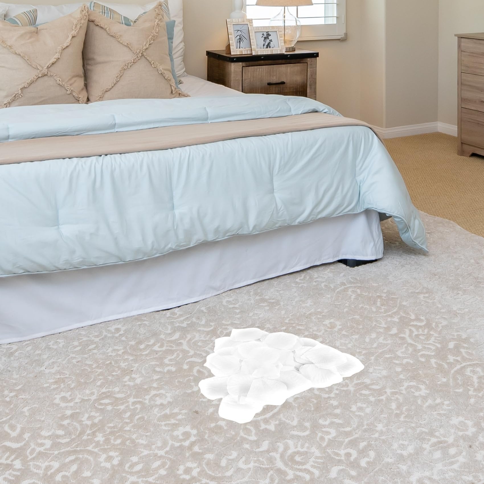 Pile of white artificial rose petals scattered on a patterned rug in a bedroom setting.