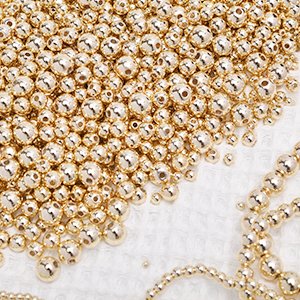 Pile of small, round, gold-colored spacer beads with holes for jewelry making.
