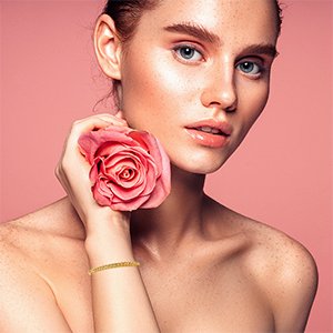 Woman with a pink rose and a gold-filled brass spacer bead bracelet on her wrist against a pink background