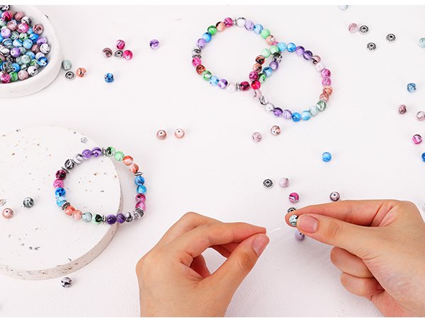 Hands stringing colorful 8mm ink pattern acrylic craft beads onto crystal string to make bracelets