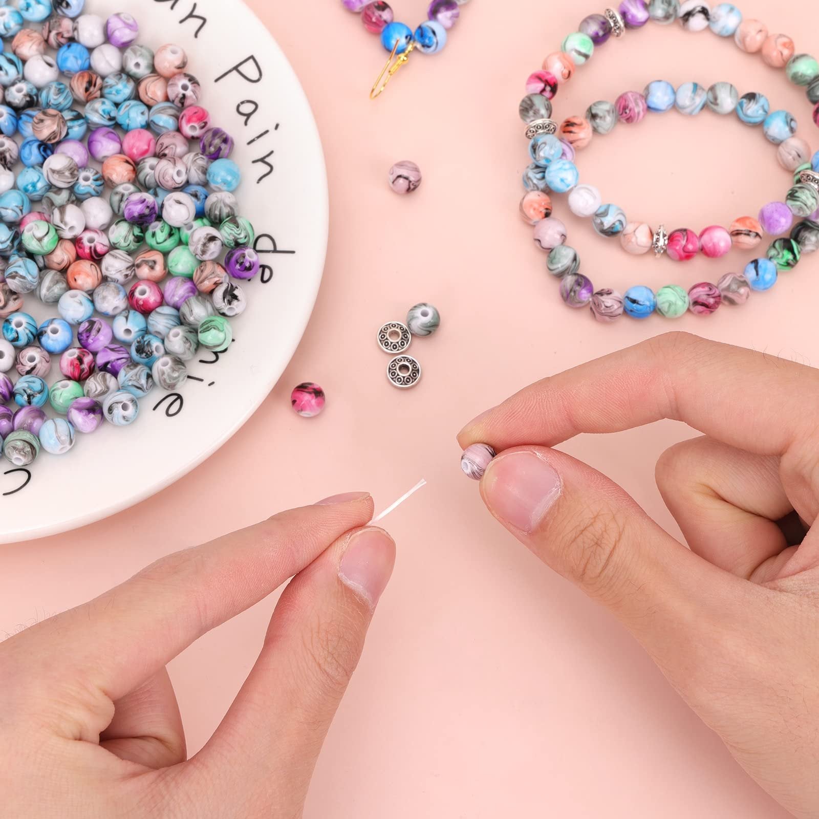 Hands stringing colorful ink pattern acrylic beads onto crystal string for jewelry making