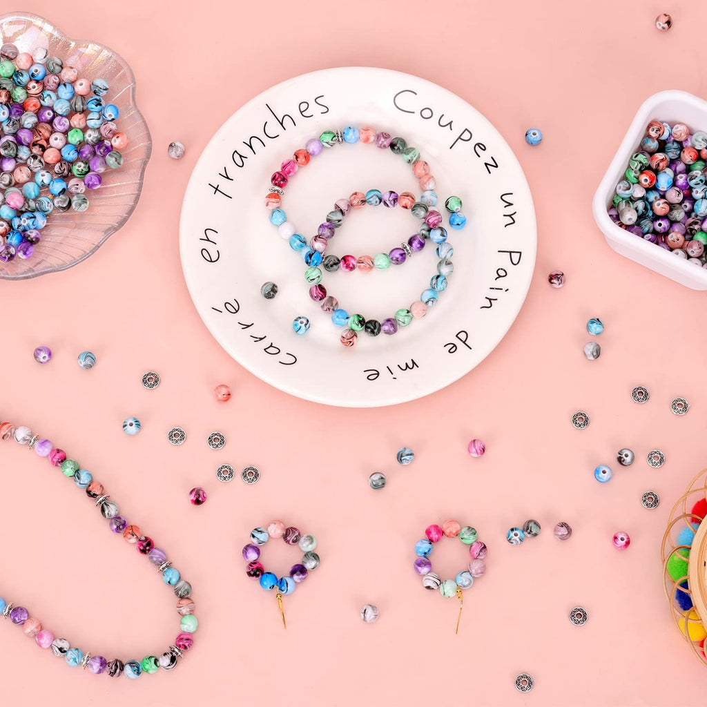 Assorted colorful ink pattern craft beads scattered on a pink background with bracelets and a decorative plate.