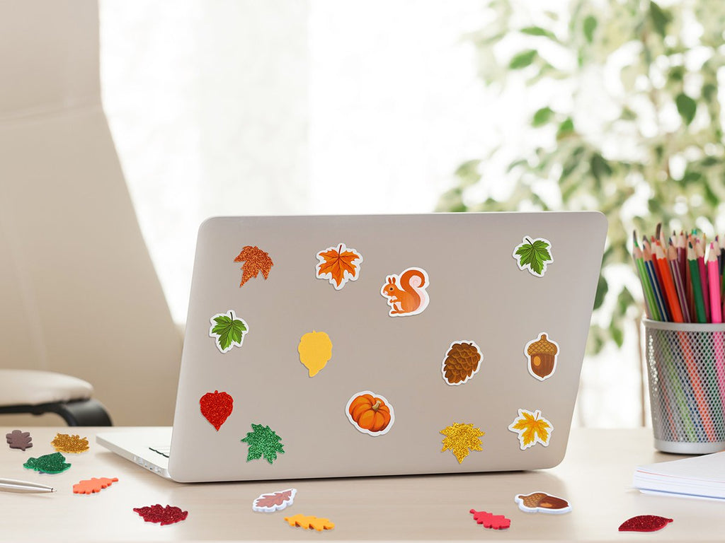 Fall leaf and animal foam stickers decorating a laptop on a desk with pencils and notebooks.