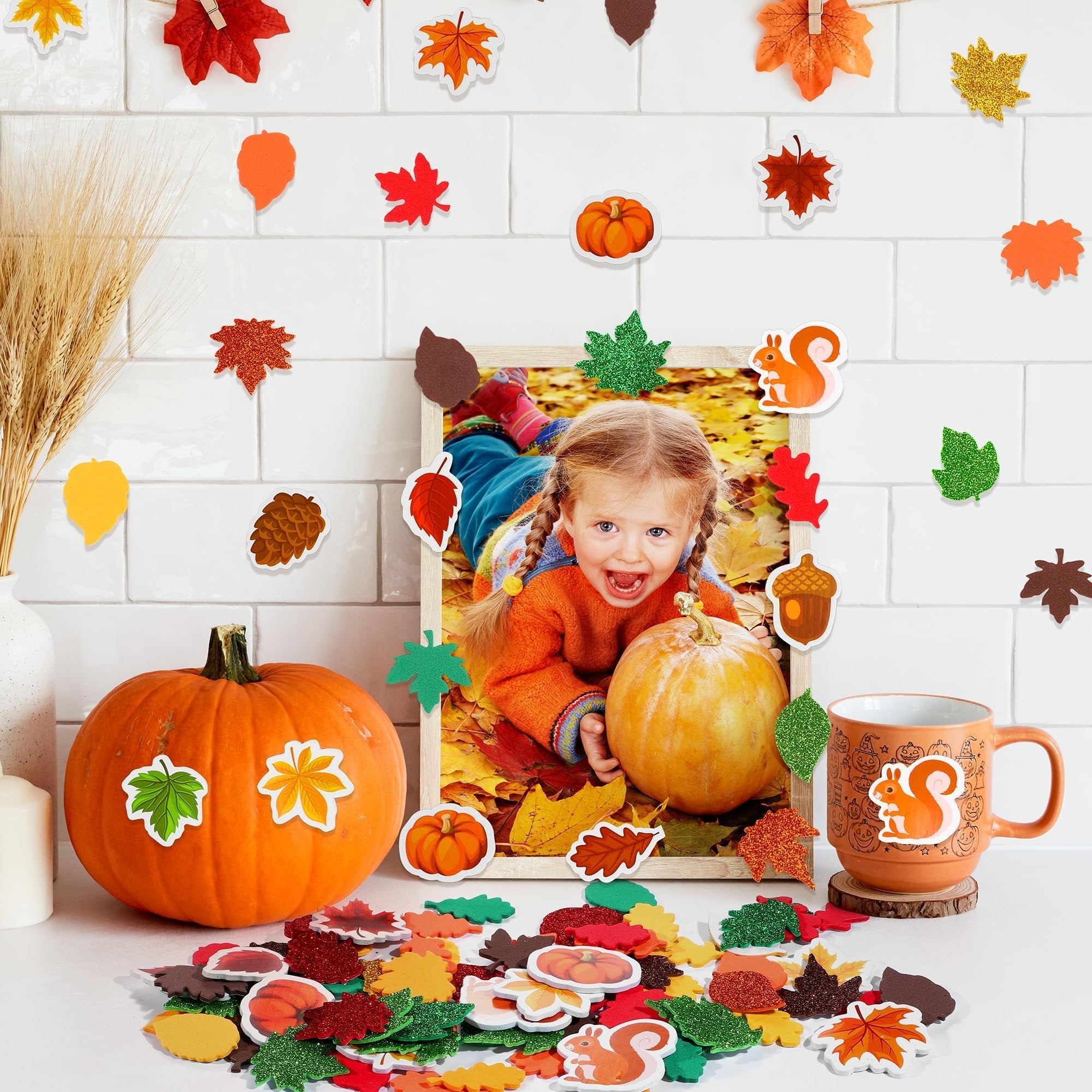 Fall leaf foam stickers scattered around a pumpkin and a framed photo of a child, with wheat stalks and a mug.