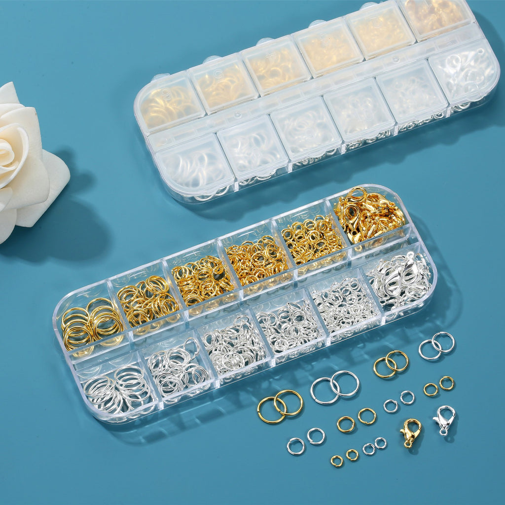 Two clear storage boxes filled with gold and silver jump rings and lobster clasps, with loose rings and clasps scattered on a blue surface.