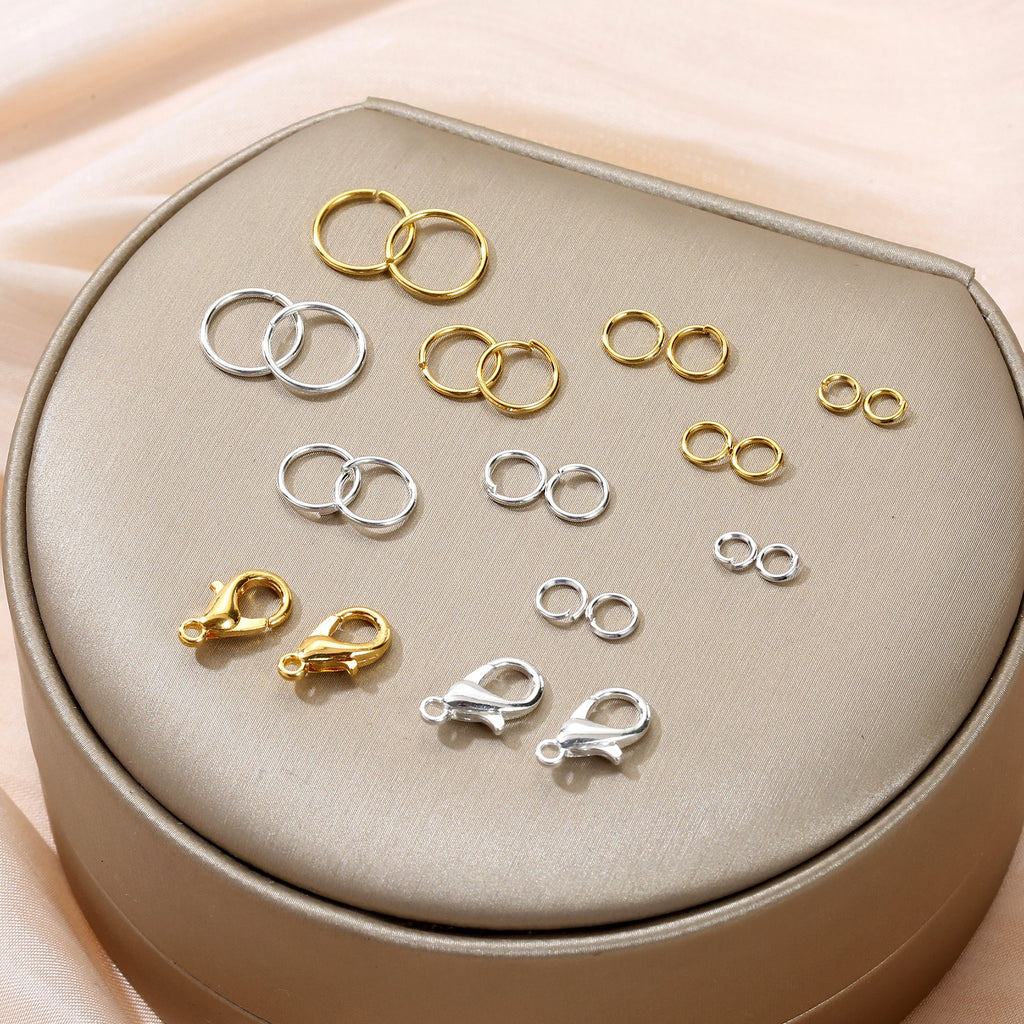 Assortment of gold and silver jump rings and lobster clasps displayed on a textured surface.
