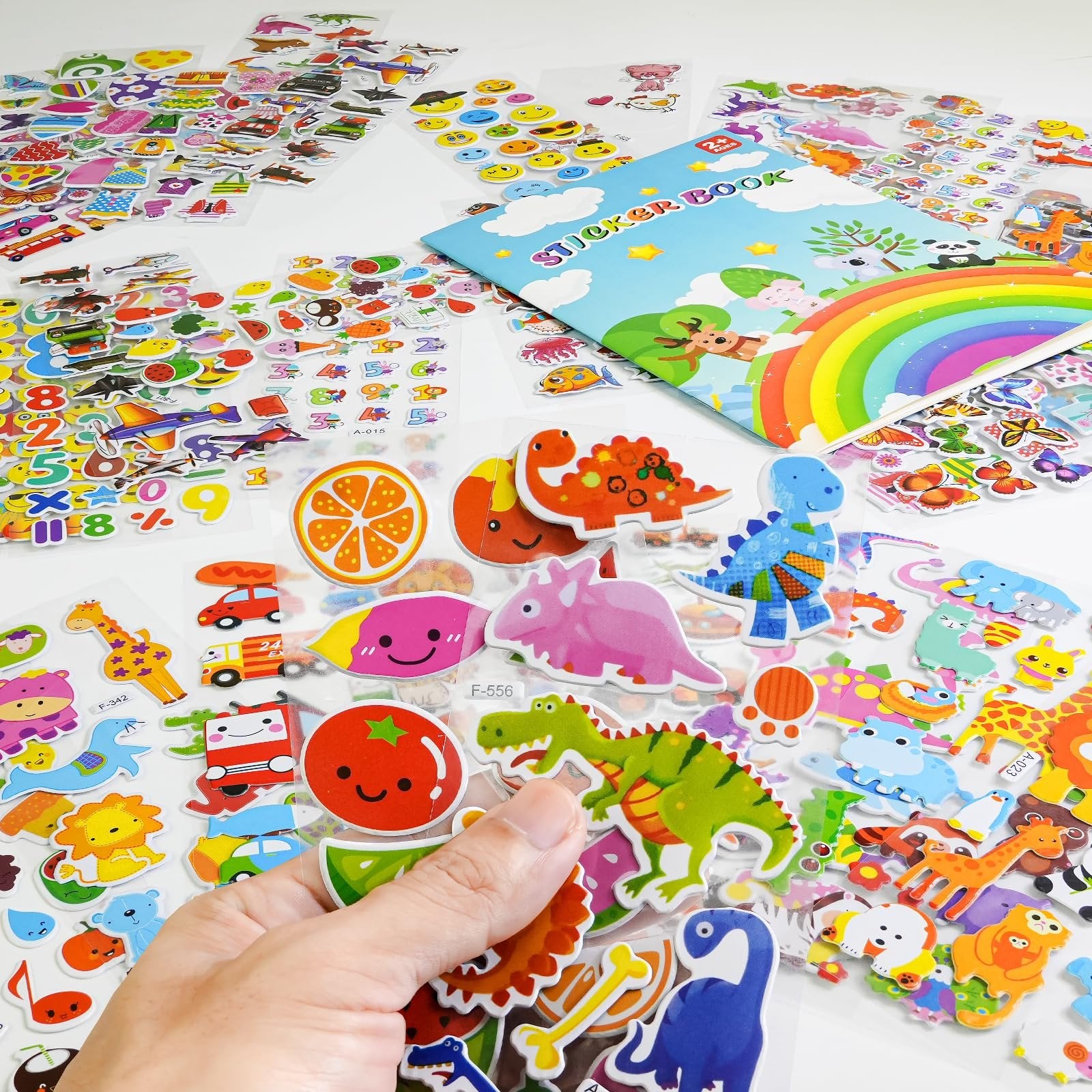 Hand holding a sheet of puffy stickers featuring dinosaurs, animals, and vehicles, with a sticker book in the background.
