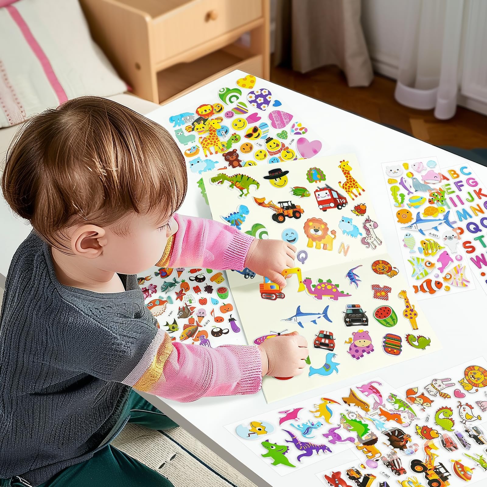 Toddler girl applying puffy stickers of animals, vehicles, and letters to sticker books on a white table.