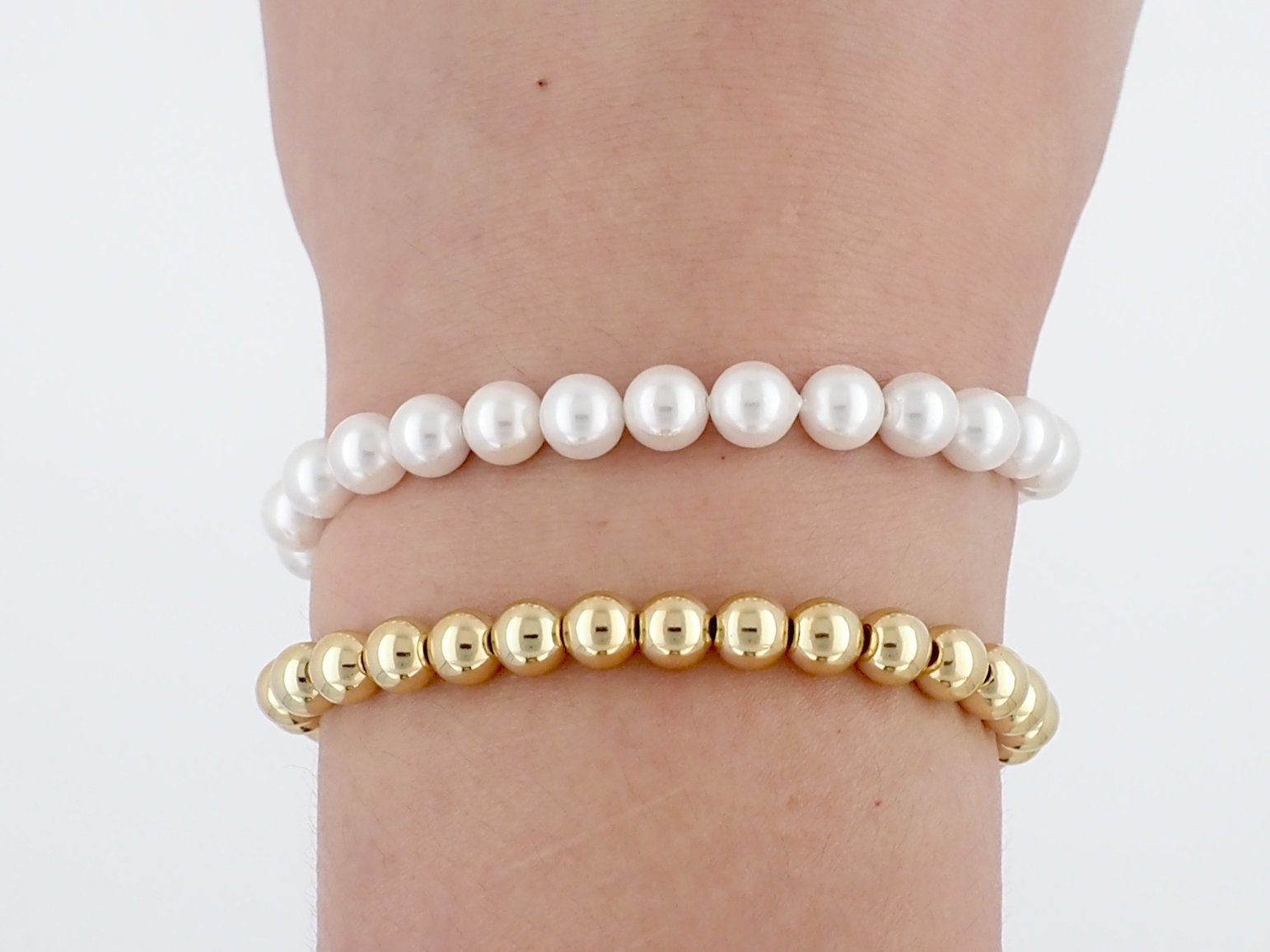 Two beaded bracelets on a wrist, one with white pearls and one with gold beads.