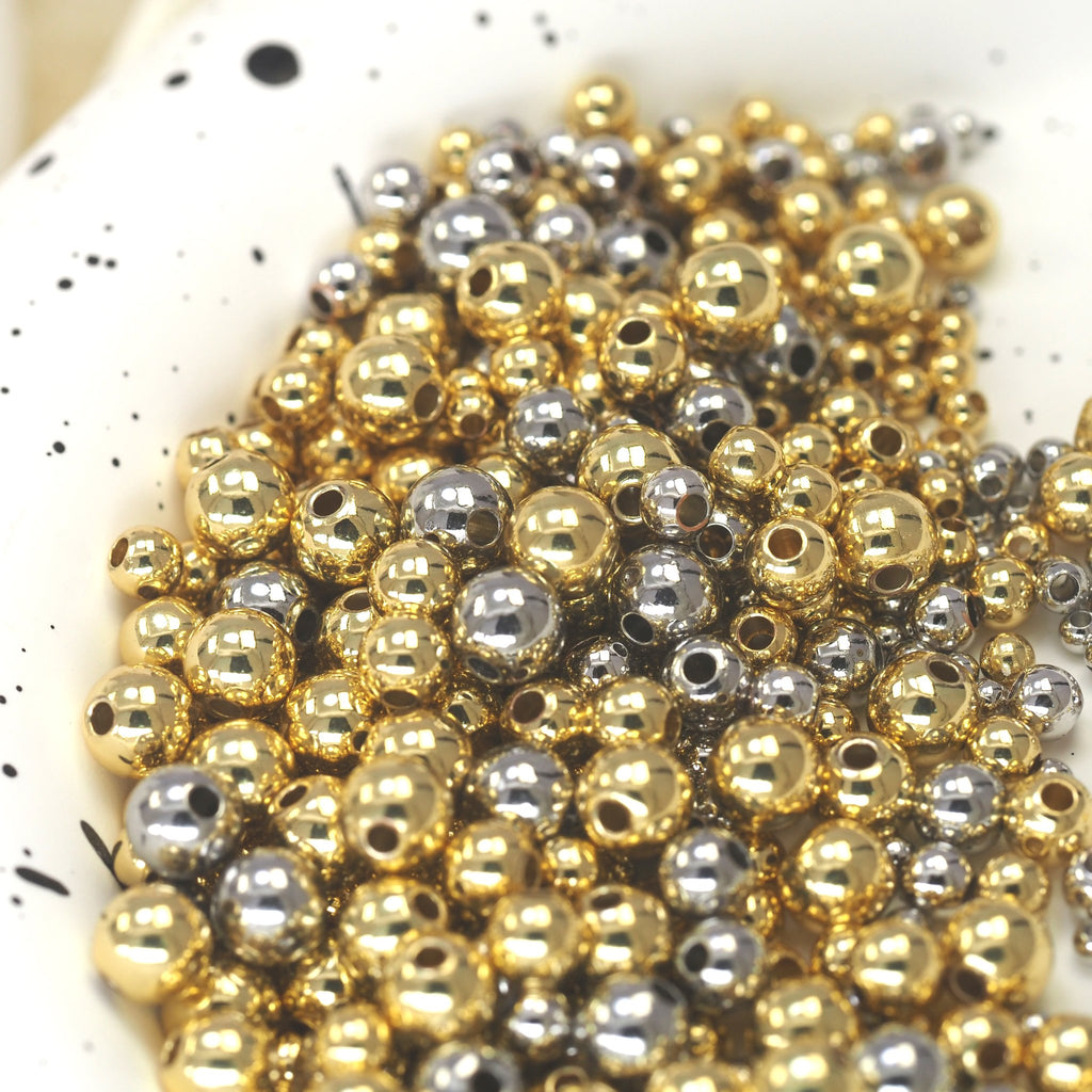 Close-up of a pile of small gold and silver round spacer beads with holes for jewelry making, scattered in a speckled white dish.