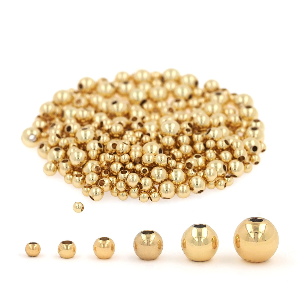 Pile of smooth round gold-filled brass spacer beads with a row of different sized beads shown below on a white background.