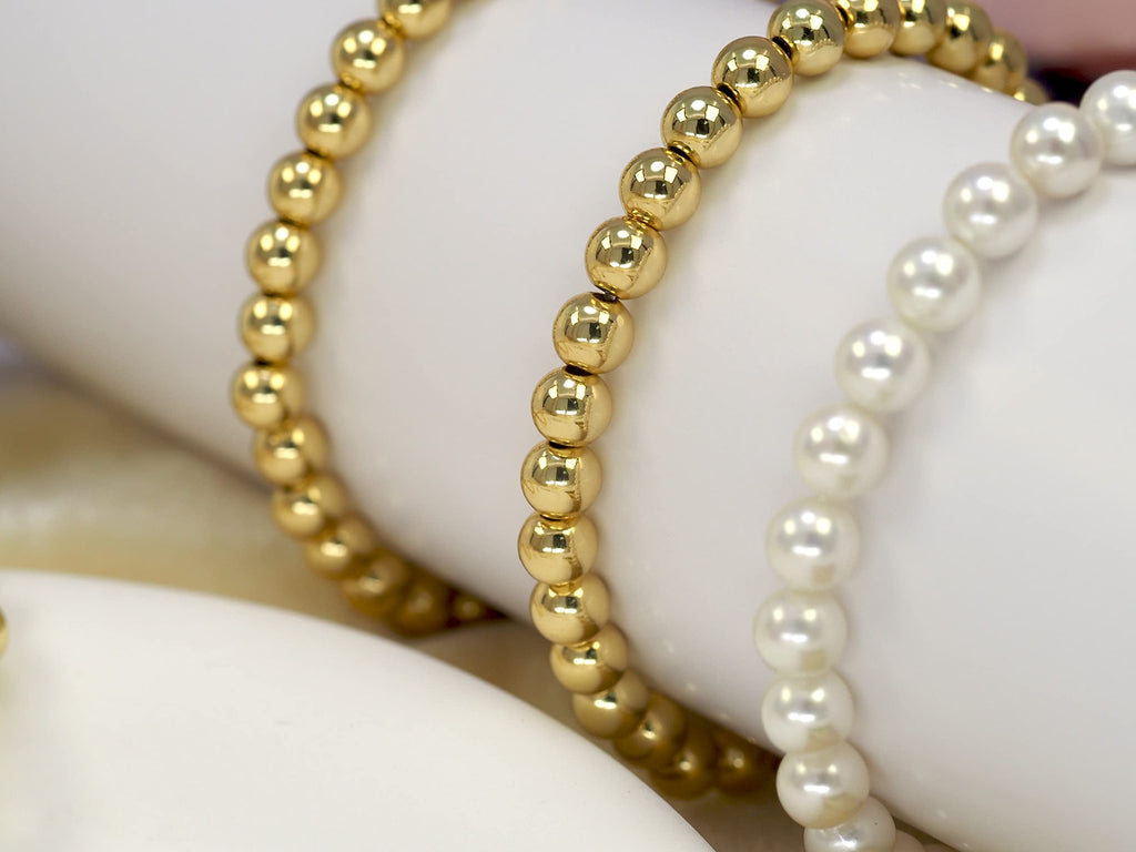 Close-up of gold and pearl beaded bracelets on a white surface, showing the texture and shine of the beads.